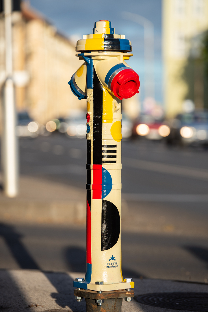 A képen a színes, sárga, piros Bauhaus stílusú mintákkal festett tűzcsap látható.